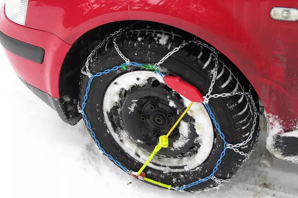 Auto rojo siguiendo el Consejos para Conducir con Nieve al colocar cadenas en neumáticos