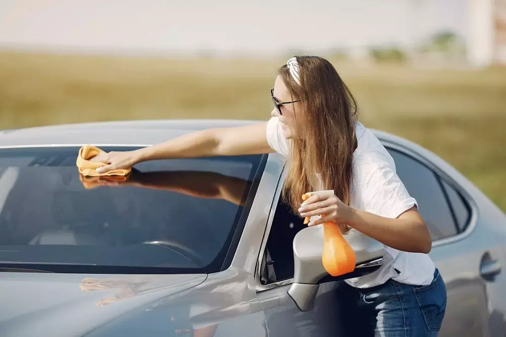 Mujer limpiando parabrisas de auto para seguir los Consejos para Conducir en Caminos de Tierra